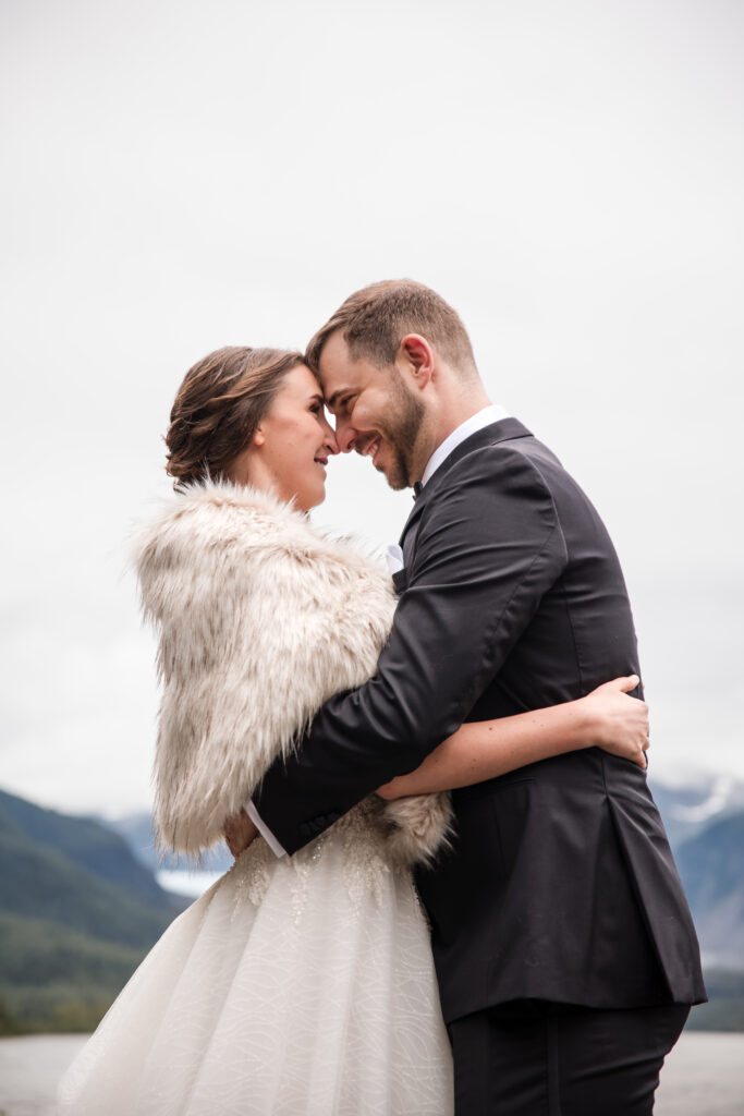 couple embraces during first look of their elopement in Juneau, Alaska with Mendenhall Glacier in the background