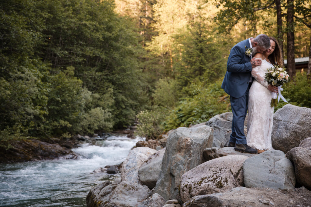 couple embrace standing on rocks next to a creek in Alaska for their elopement with Christine Johnson Photography