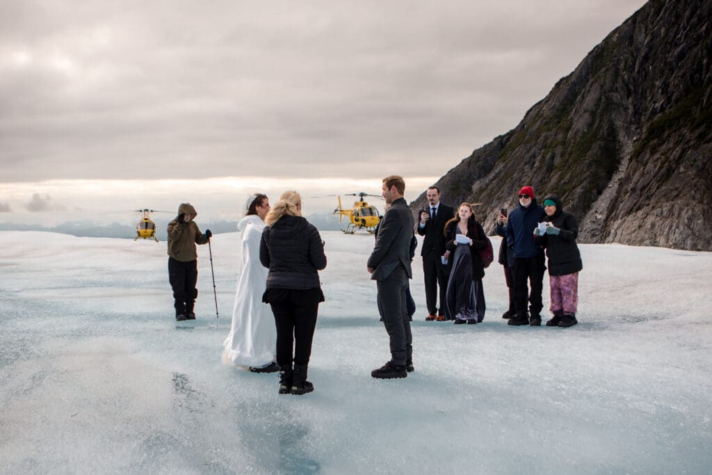 Couple exchanges vows with an officiant and guests on glacier ice during a Juneau helicopter elopement.