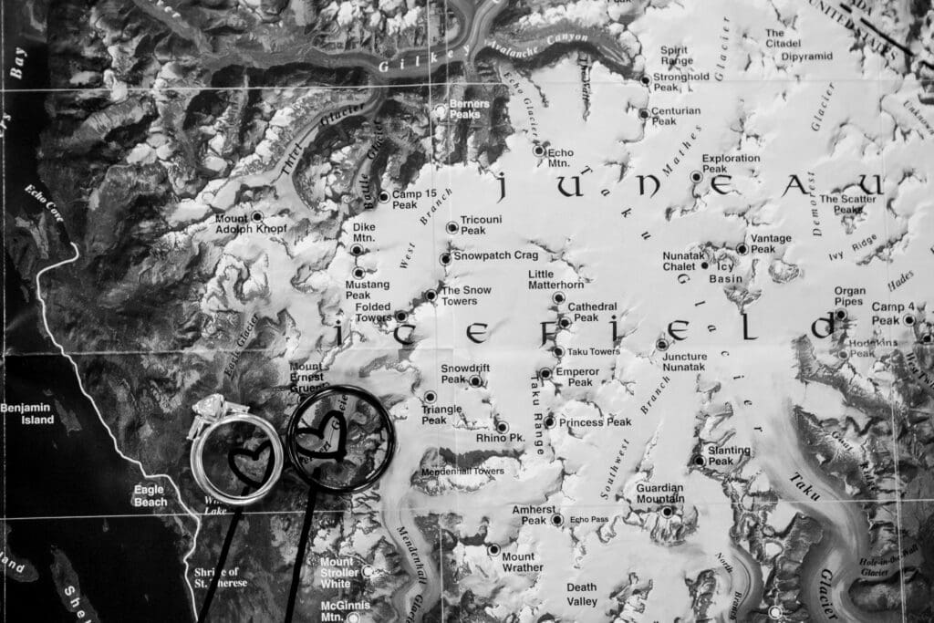 Black-and-white close-up of wedding rings resting on a map of the Juneau Icefield.
